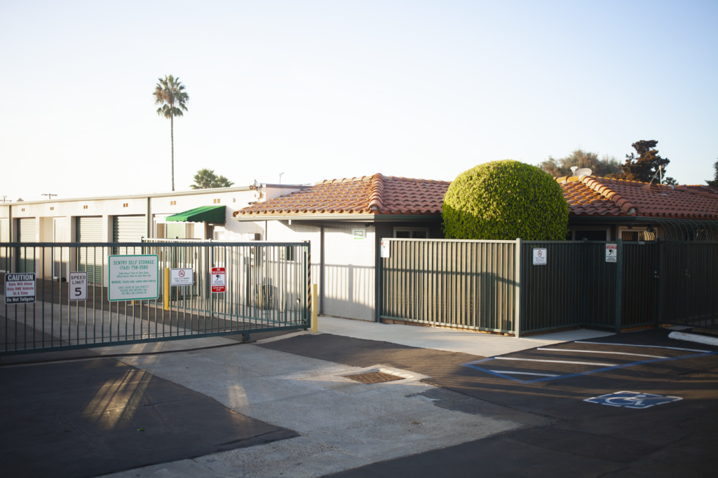 a gated parking lot with a building and a tree